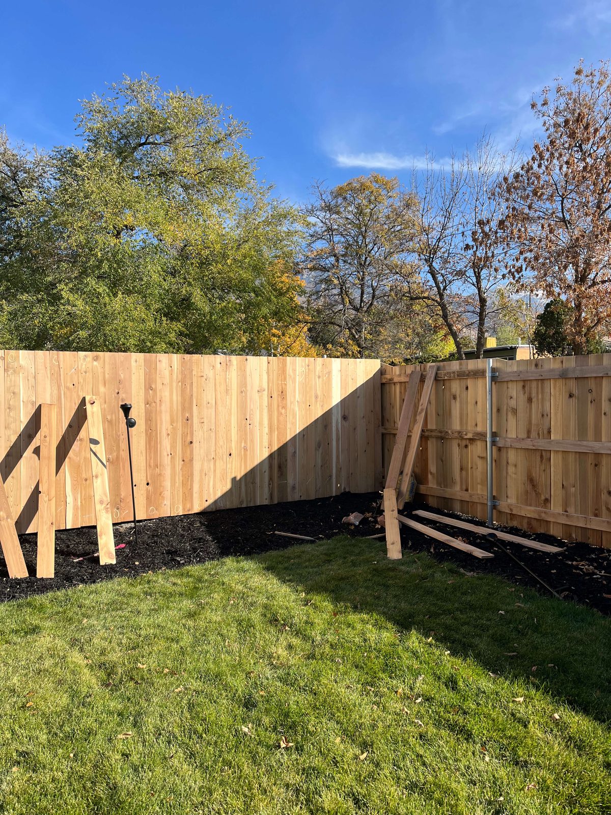 Corner of a new cedar fence run with panels staged and a steel corner upright set in concrete