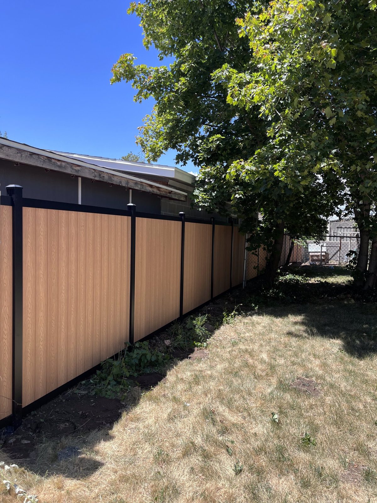 Light brown vertical composite privacy fence with black aluminum posts along the side of a back yard in the Salt Lake Valley, installed by Trusted Fence
