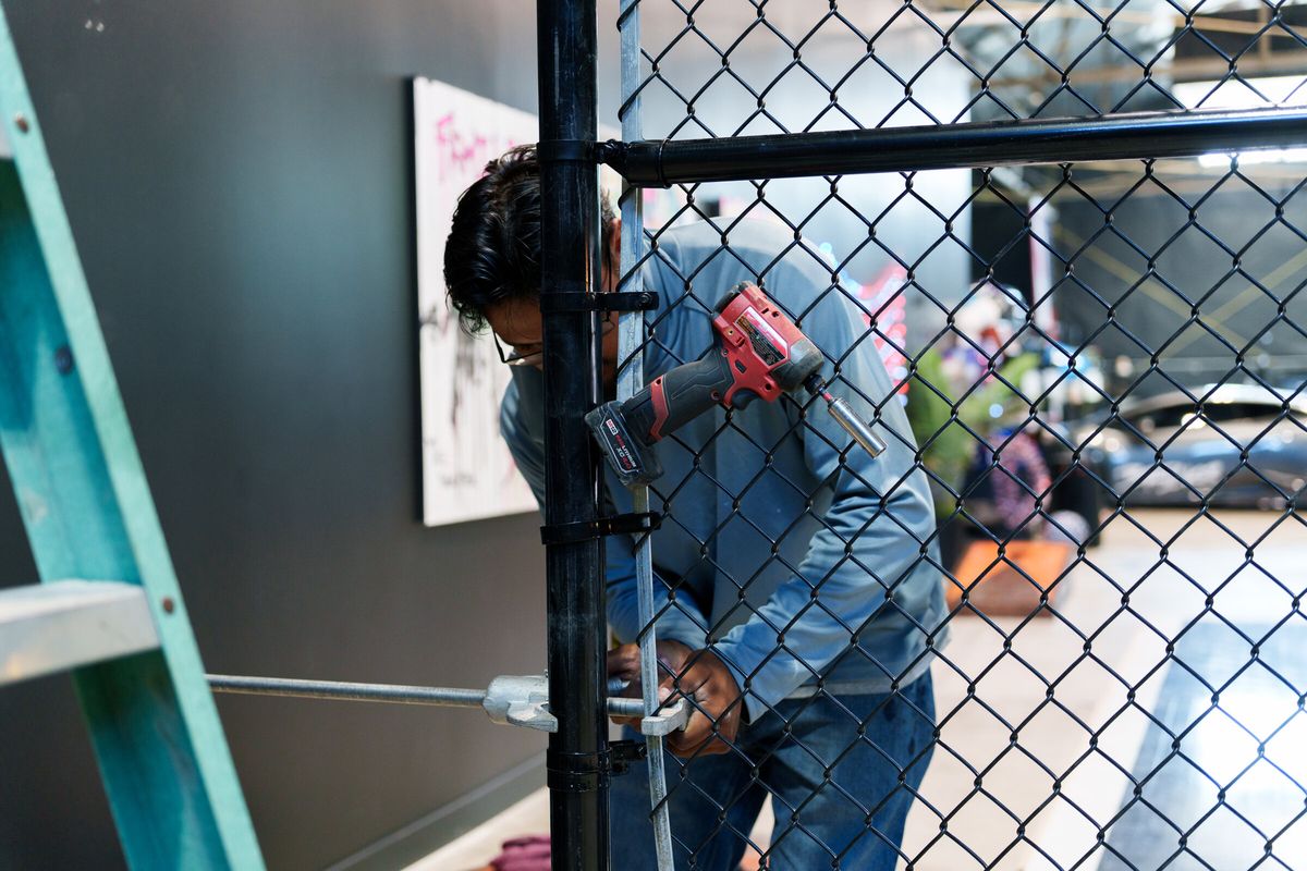 Crew member fastening black chain link mesh to a post while installing a sports cage in Salt Lake City, UT