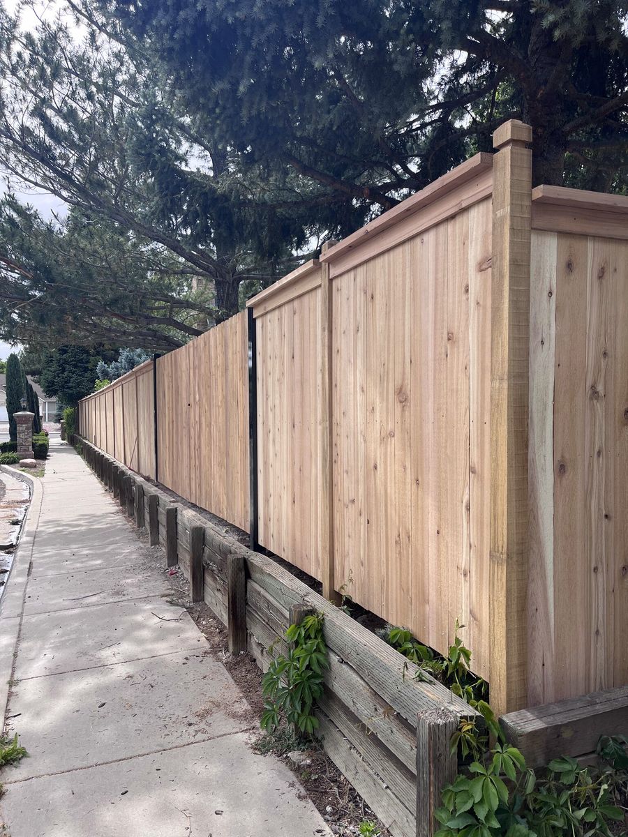 Capped cedar privacy fence turning a corner above a timber retaining wall along a sidewalk in Millcreek, UT