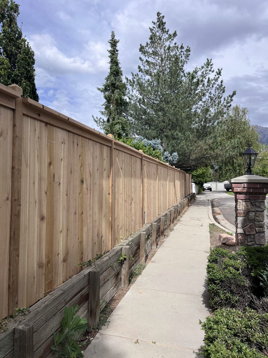 Cedar privacy fence with a top cap running along a sidewalk above a timber retaining wall in Millcreek, UT