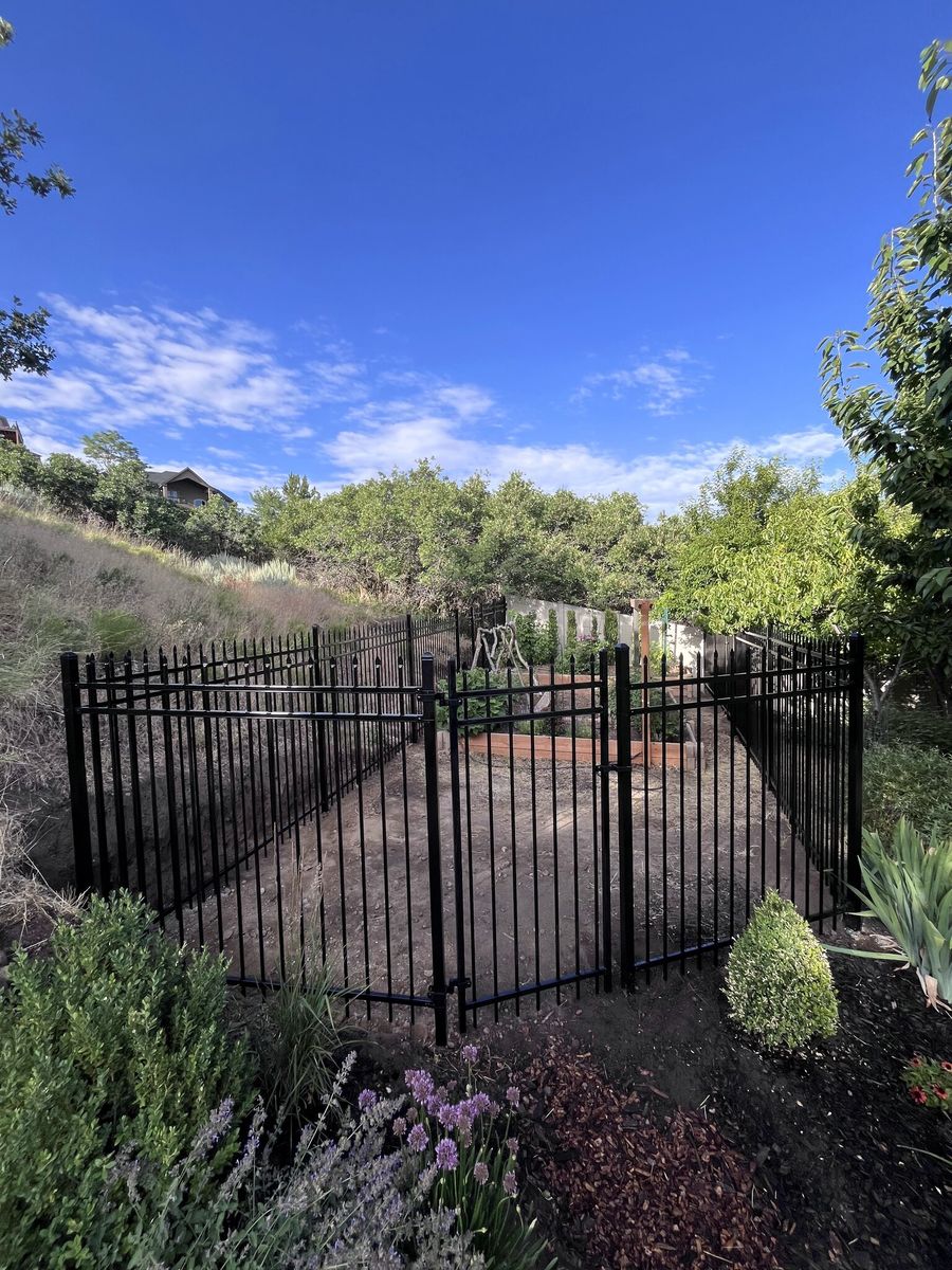 Black ornamental iron double gate and fence enclosing a backyard garden in Sandy, UT