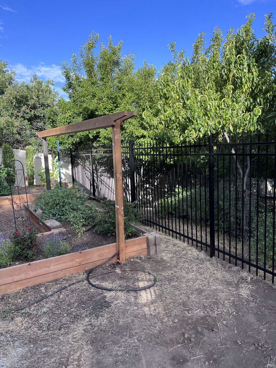 Black ornamental iron garden fence beside a wooden arbor and raised beds in Sandy, UT