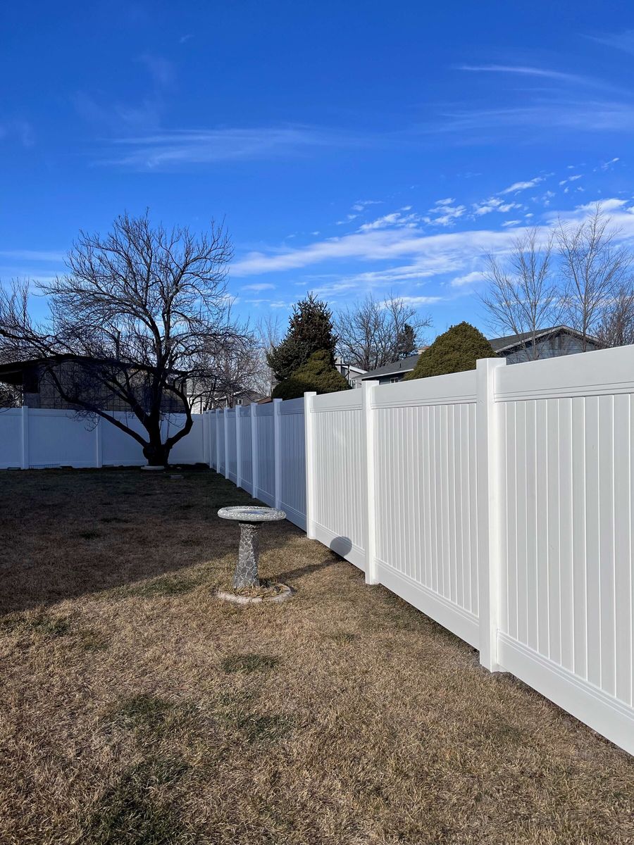 White vinyl privacy fence running along a backyard with a birdbath and bare trees in West Valley City, UT